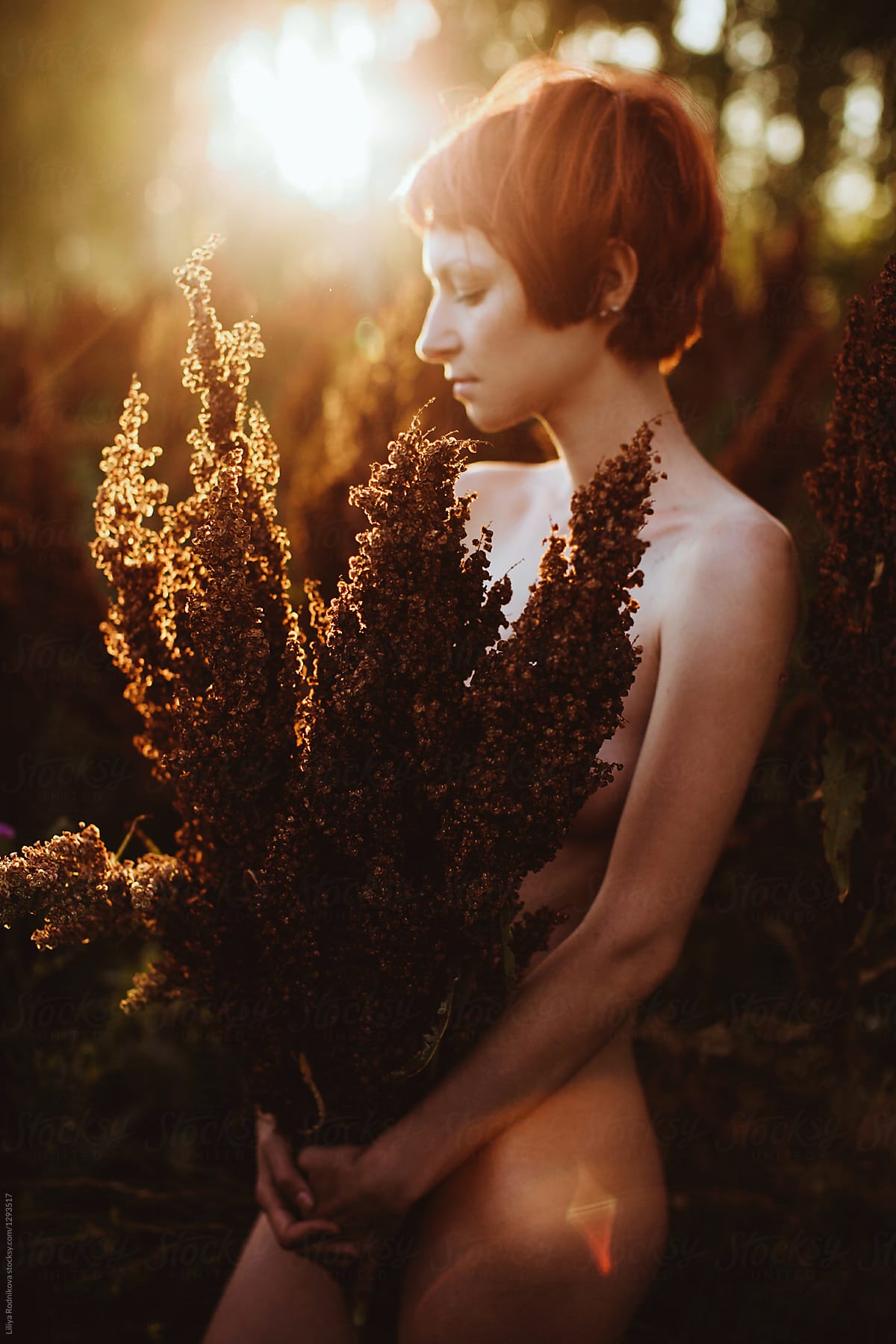 Naked young female in sunset light holding the bouquet