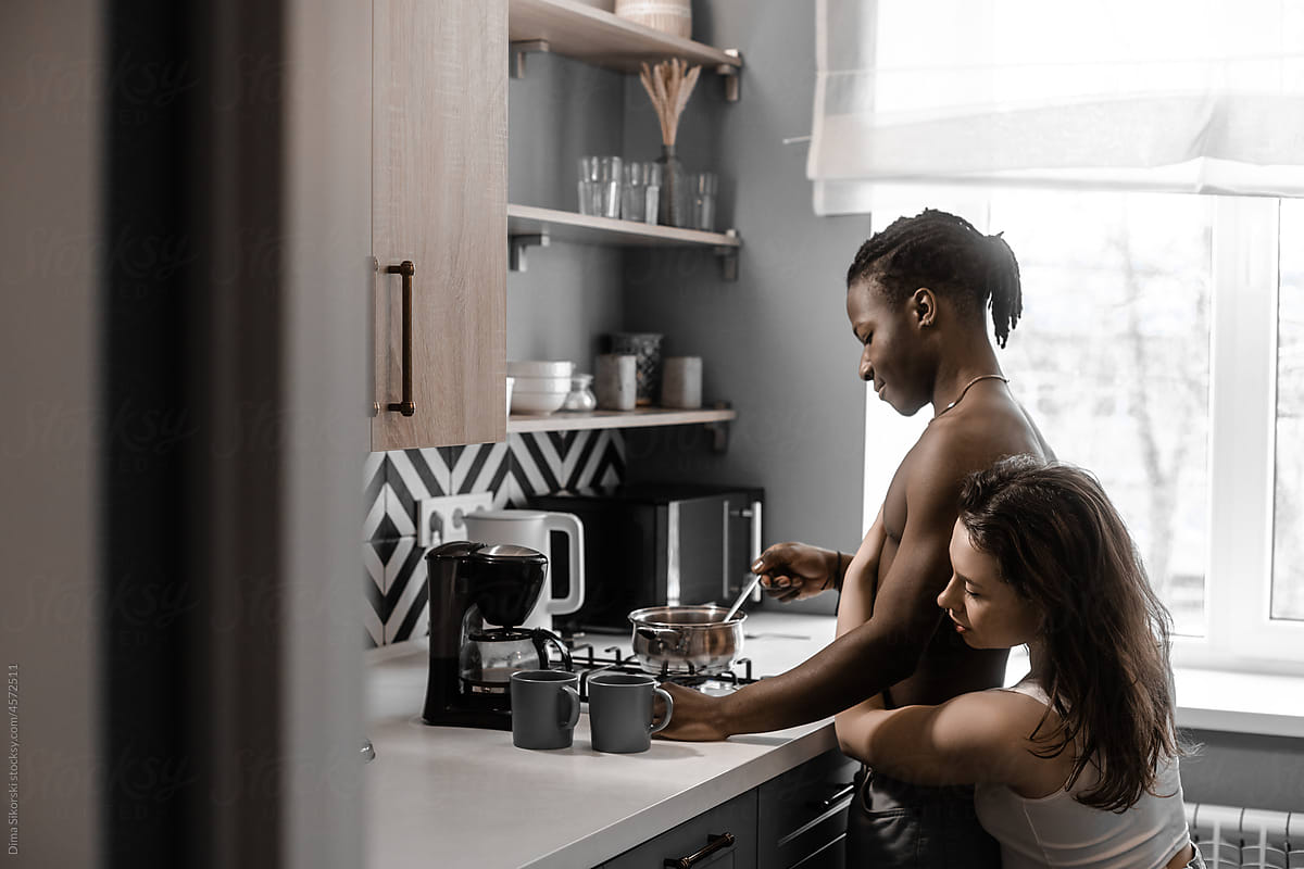 A girl in love hugs her boyfriend who is cooking breakfast