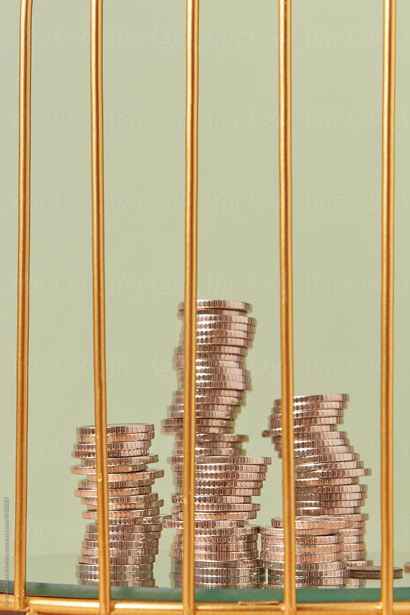 Cent coins stacks behind golden cage bars.