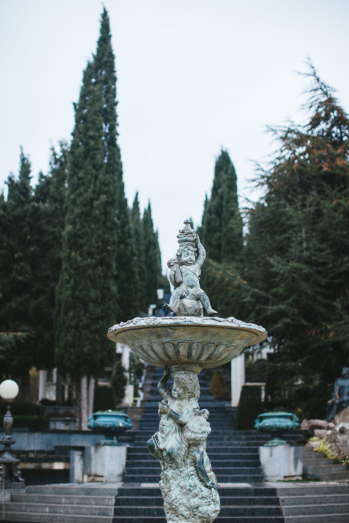 Fountain with cupids in front of stairs in the park with cypress