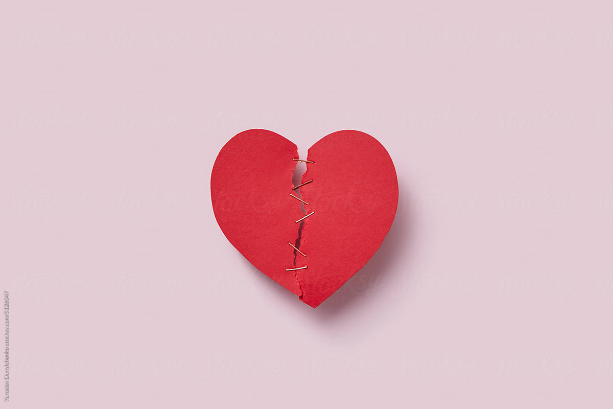 Red ripped paper cut heart on pink background.