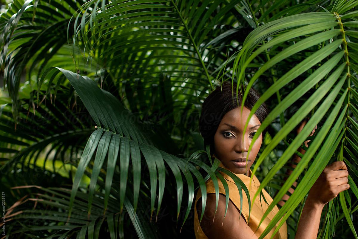Fashion Portrait of a Woman Standing by the Palm Leaves