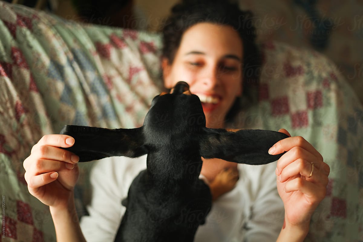 Young woman and her small black dachshund having fun on the couch. From above