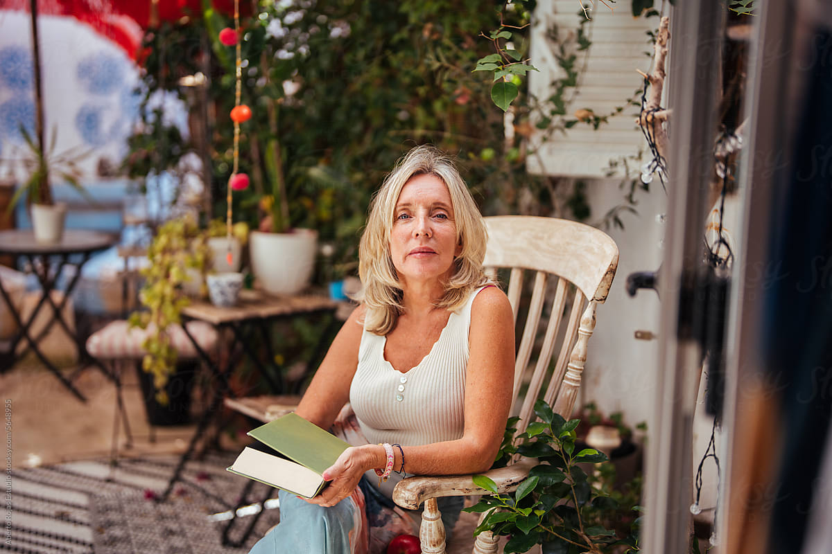 Happy mature woman sitting on armchair with book in day