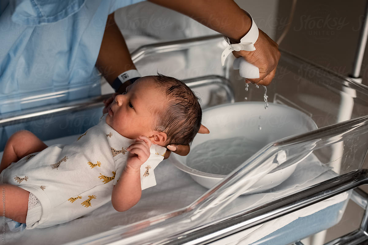 Crop African mom bathing infant in medical crib