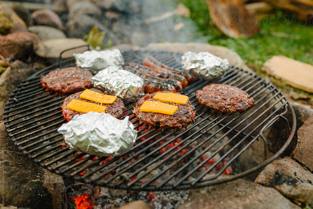 Hamburgers, sausages and baked potatoes on a grill