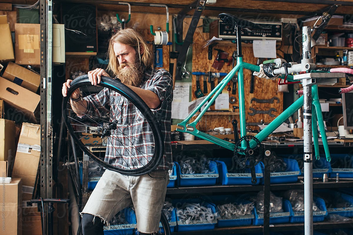 Long-Haired Hipster Mechanic Assembling Tire on Wheel of Fixed Gear Bike in Bright Workshop