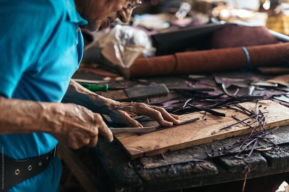 Hispanic senior shoemaker cutting leather