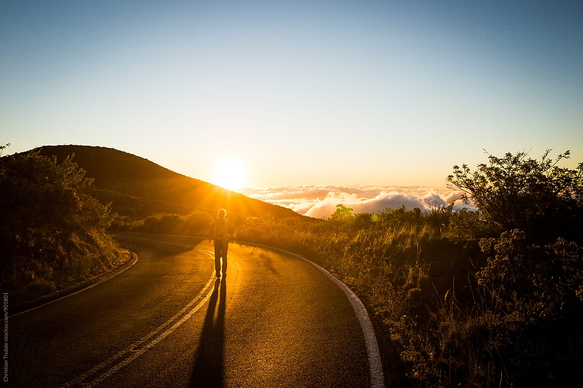 Person walking down road towards sunset on a mountainside