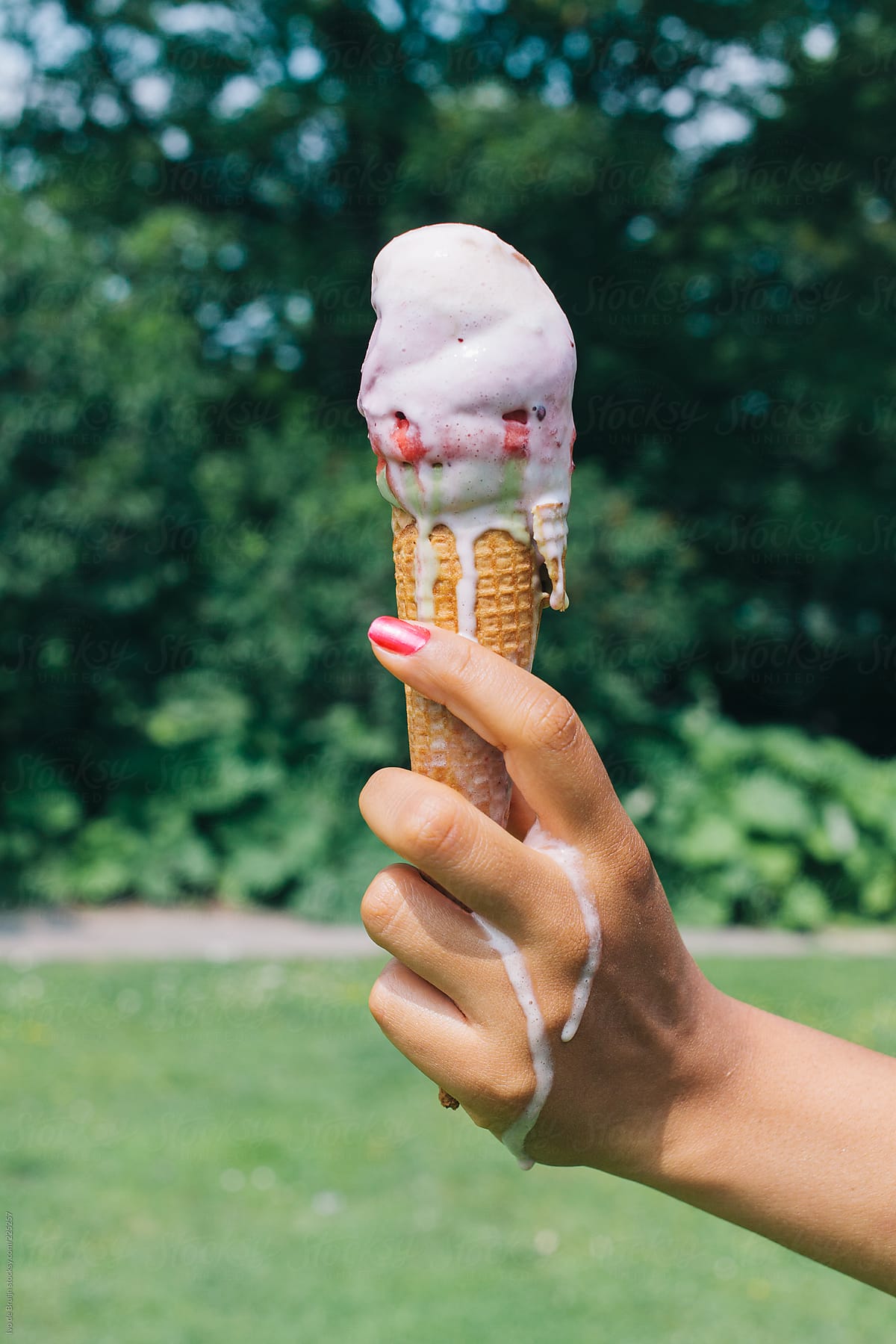 A woman's hand holding a melting colourful icecream in her hand