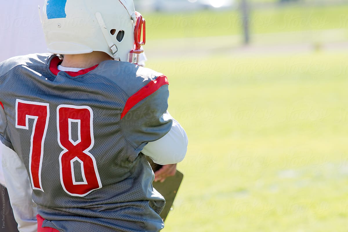 Young football player stands on sideline watching game