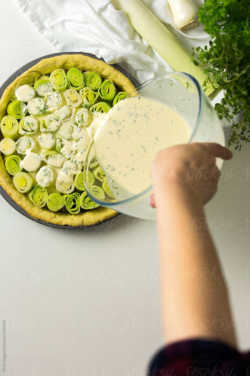 Woman pouring cream and cheese mix over leeks in a tart