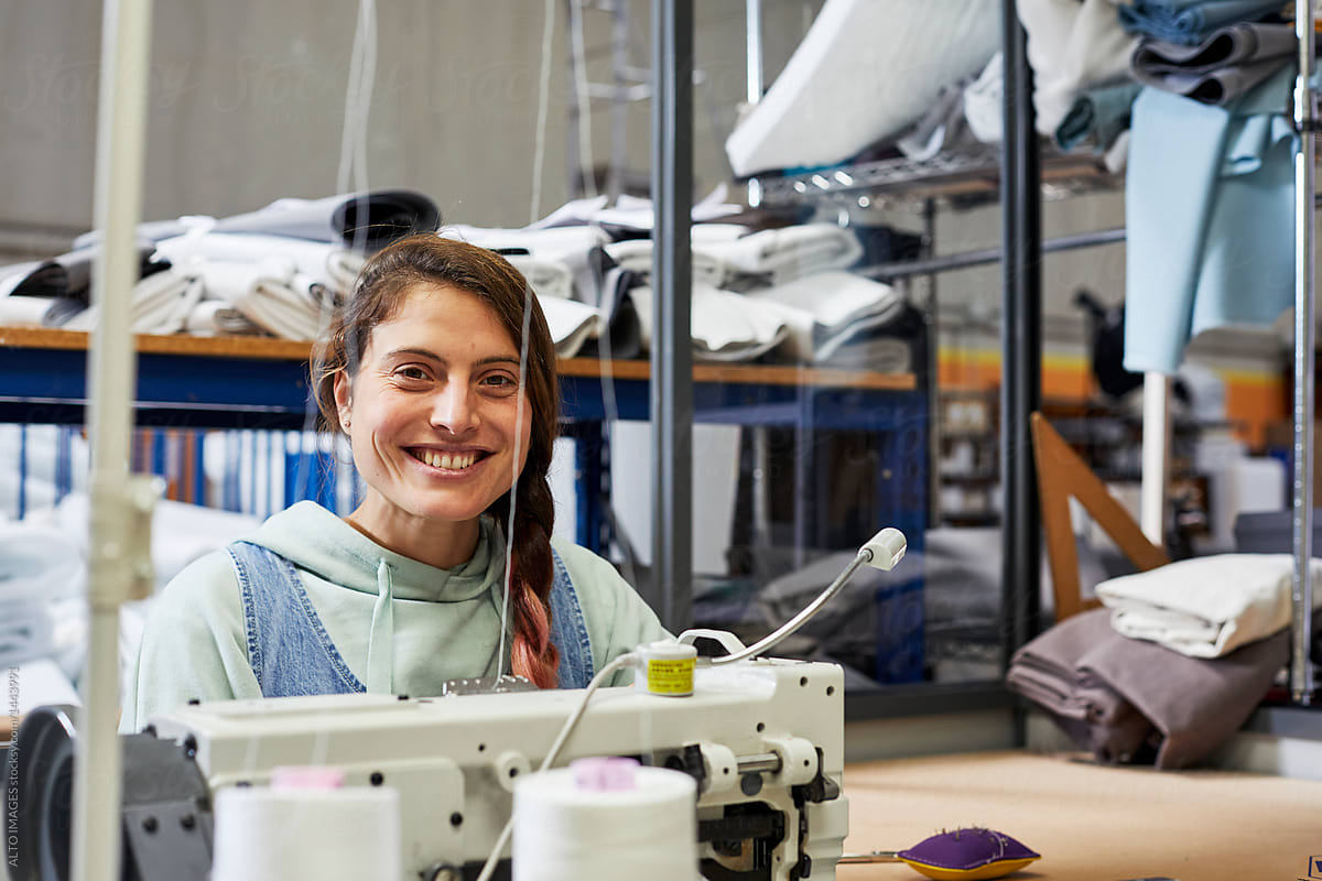 Happy Female Worker Sitting With Sewing Machine At Sofa Workshop