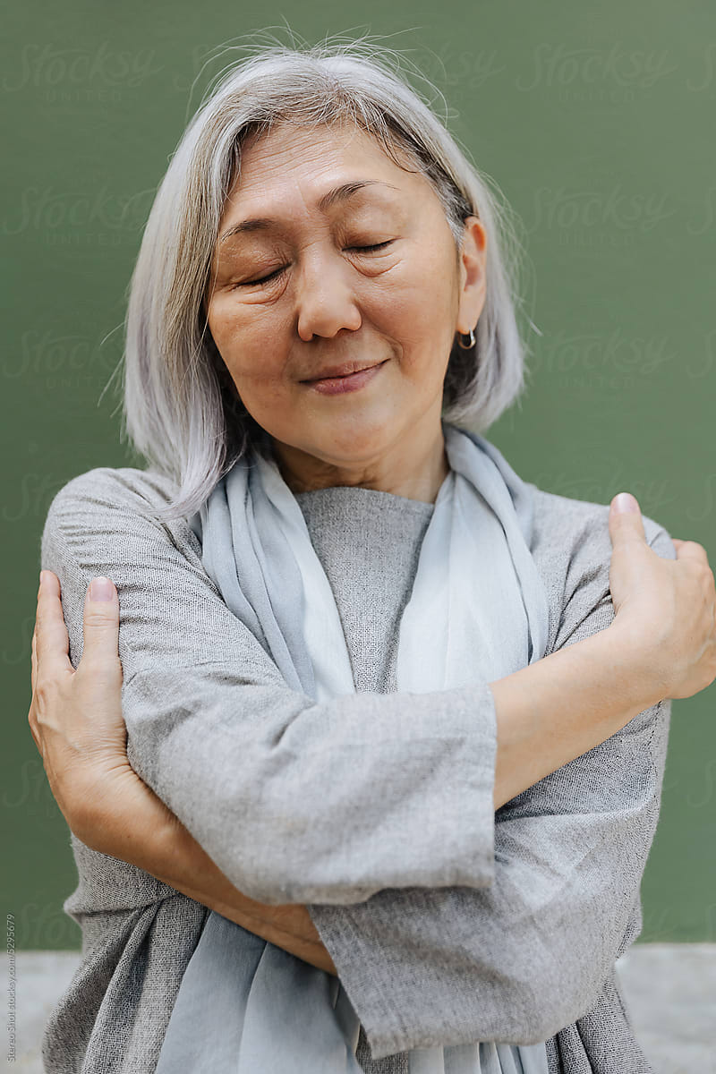 Smiling elderly woman embracing herself