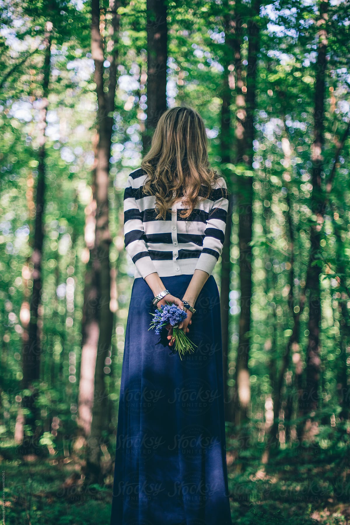 Young woman dressed in a stripped blouse and skirt in a forest from behind