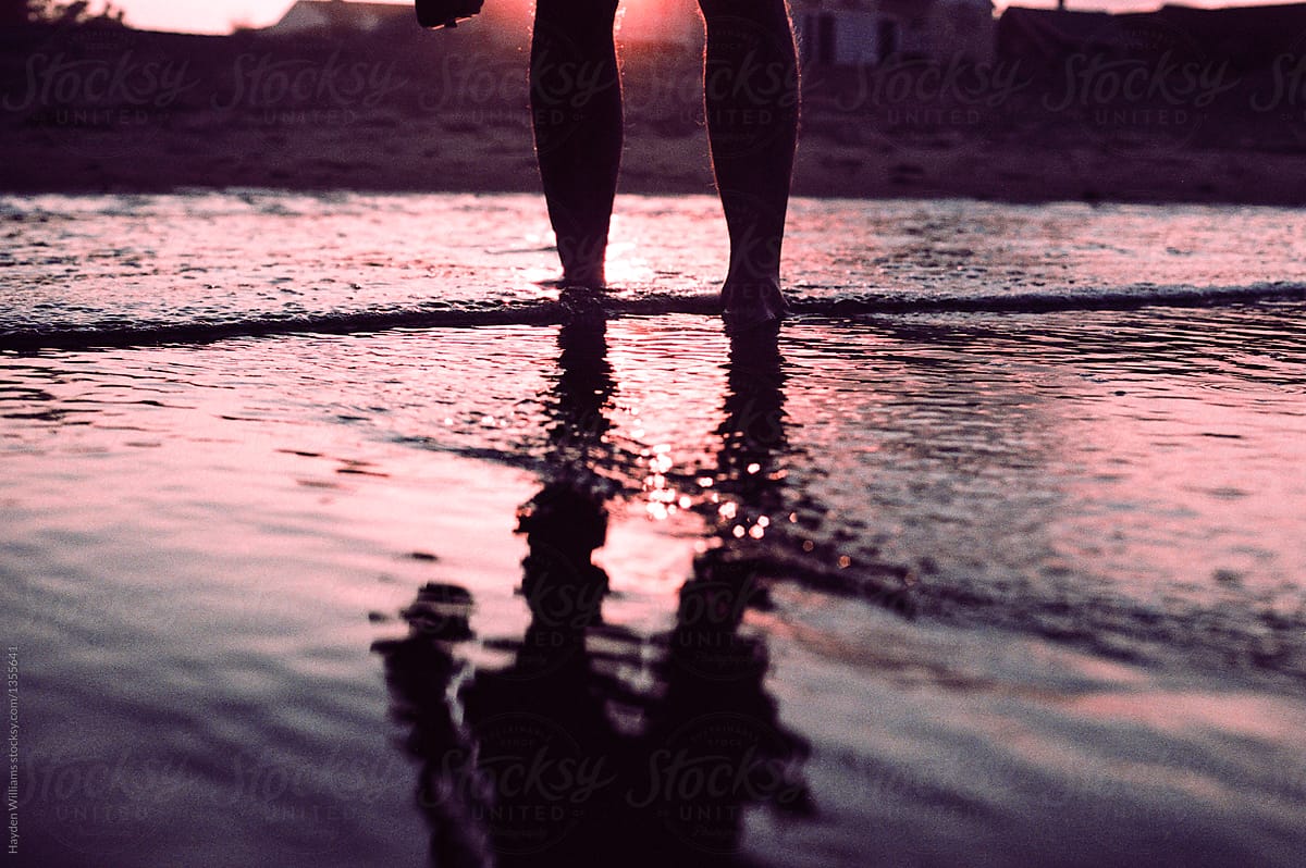 Silhouette of person\'s feet standing in ocean water by beach at sunset