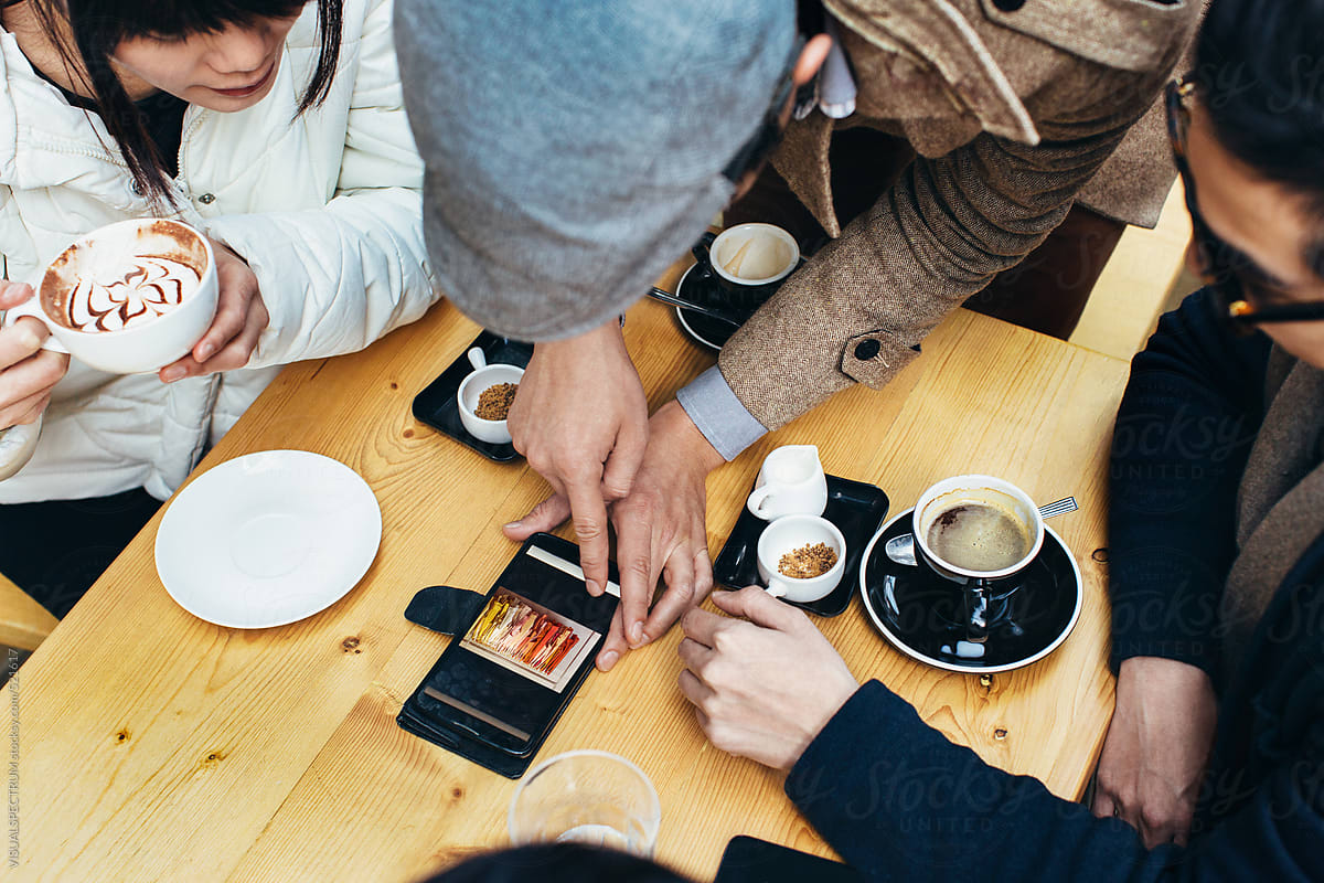 Asian Hipster Showing Fashion Photo on Cellphone to Friends in Coffee Shop