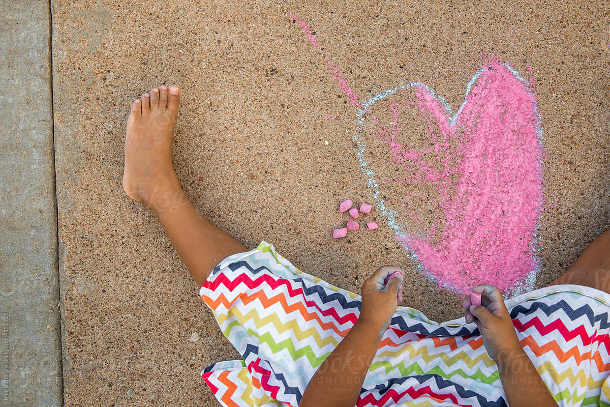 Young girl drawing chalk heart on neighborhood sidewalk