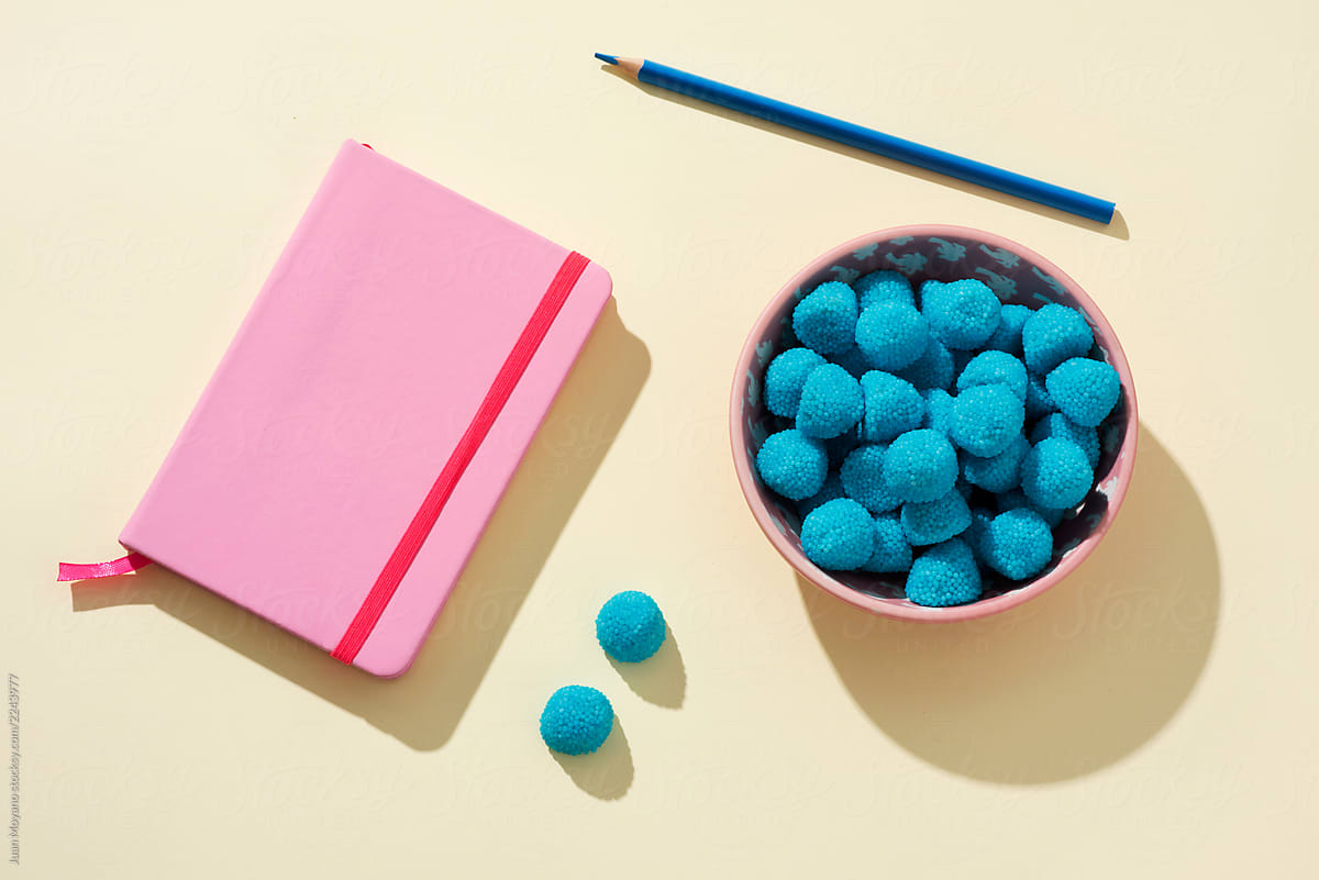 pink notepad, blue pencil and bowl with blue candies