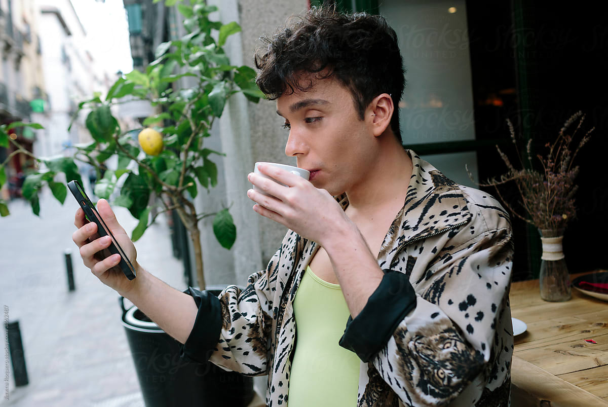 Young extravagant gay man outside a city cafeteria checking his phone