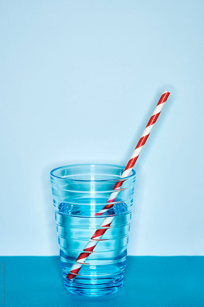 Blue glas with water and red white straw in front of blue backdrop