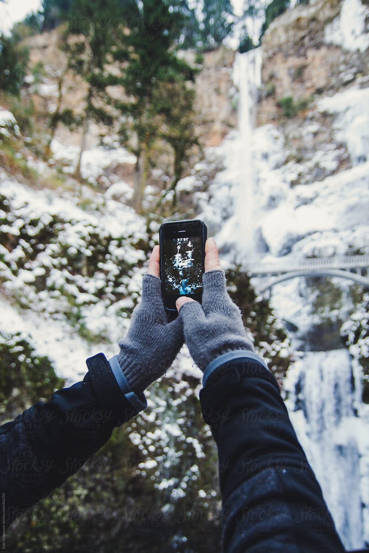 Man\'s hands taking picture of frozen Multnomah Falls with his iPhone