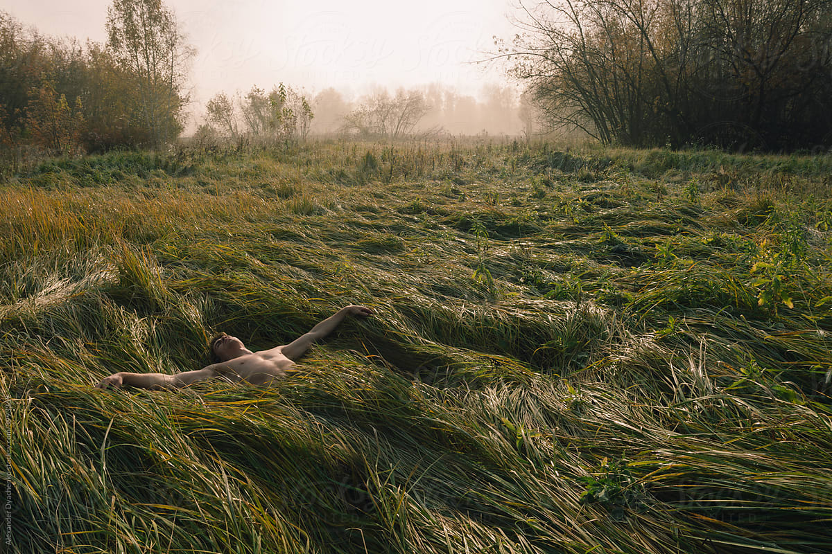 Young man lies in waving grass. Morning forest with fog