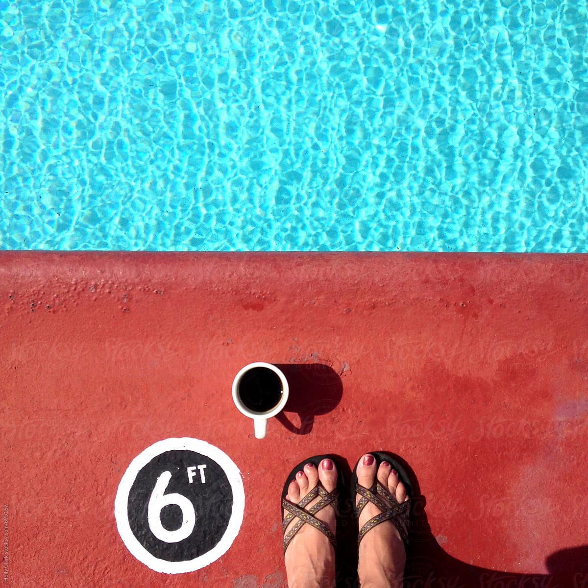 Women's feet on red concrete with a coffee cup at the pool