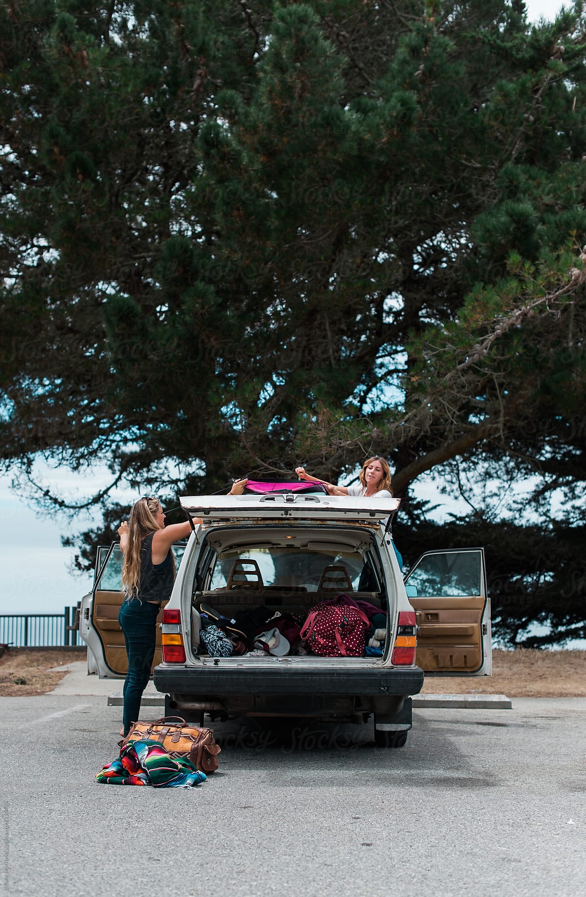 Two Young Women Unloading Surfboards from an old White Car