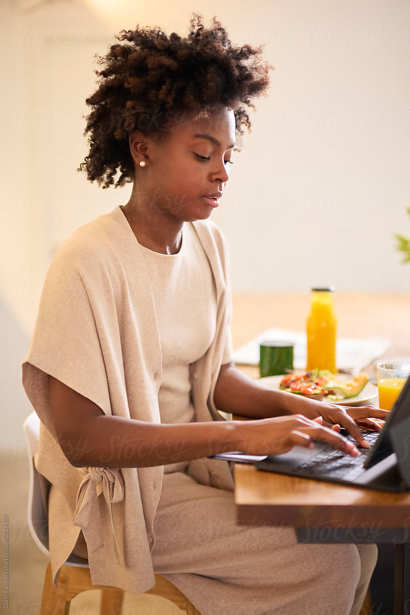 Black woman using laptop at kitchen.