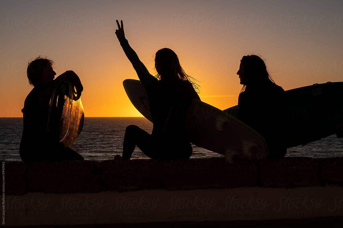 Three surfer girls looking at a sunset