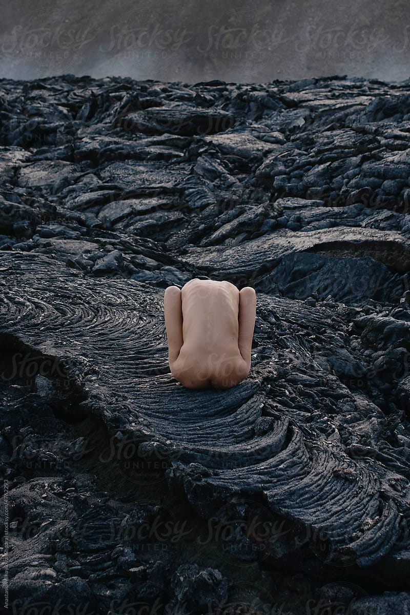 Naked female sitting leaning forward on black solid lava in Iceland