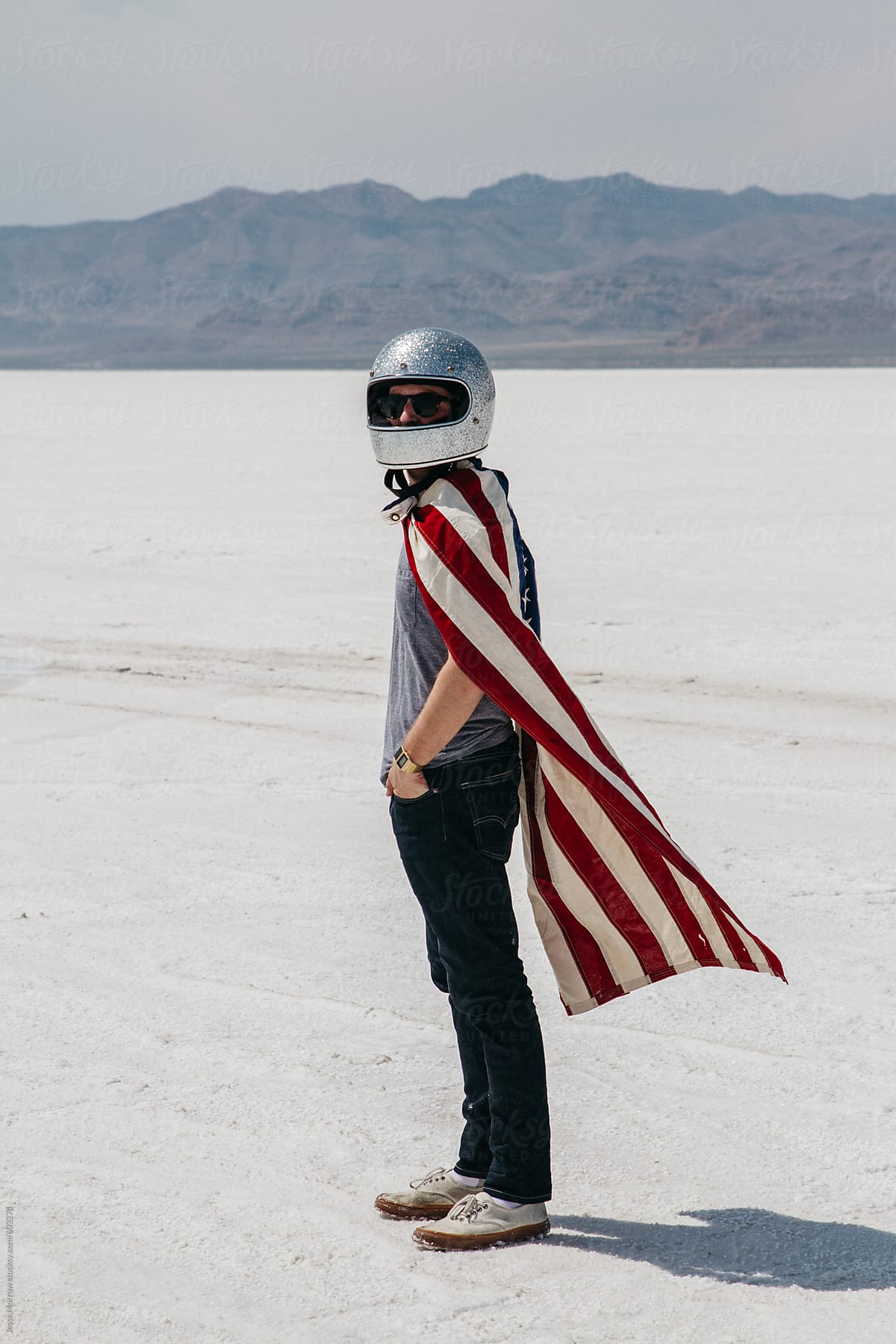 young male wearing motorcycle sparkle helmet and american flag standing in desert salt flat