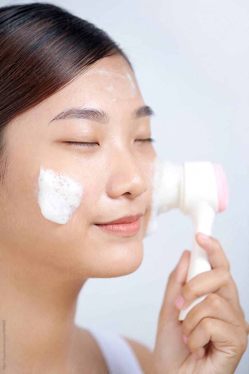 Young woman washing face with brush and cleansing foam