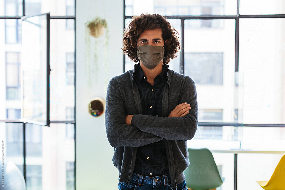 Serious man in protective mask standing near window