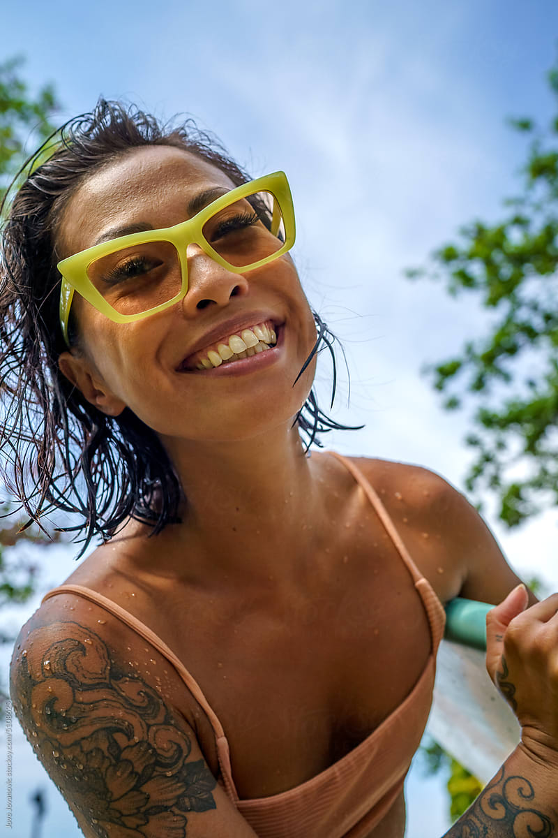 Happy woman in bikini holding surfboard against sky