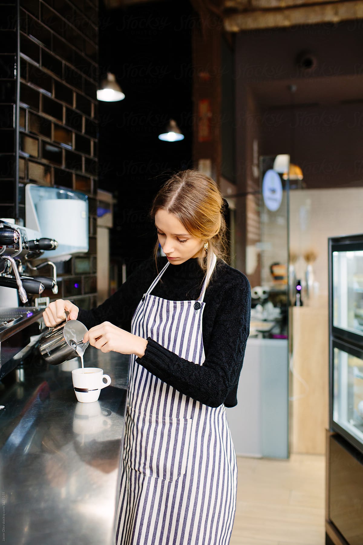 Young barista pouring milk in coffee
