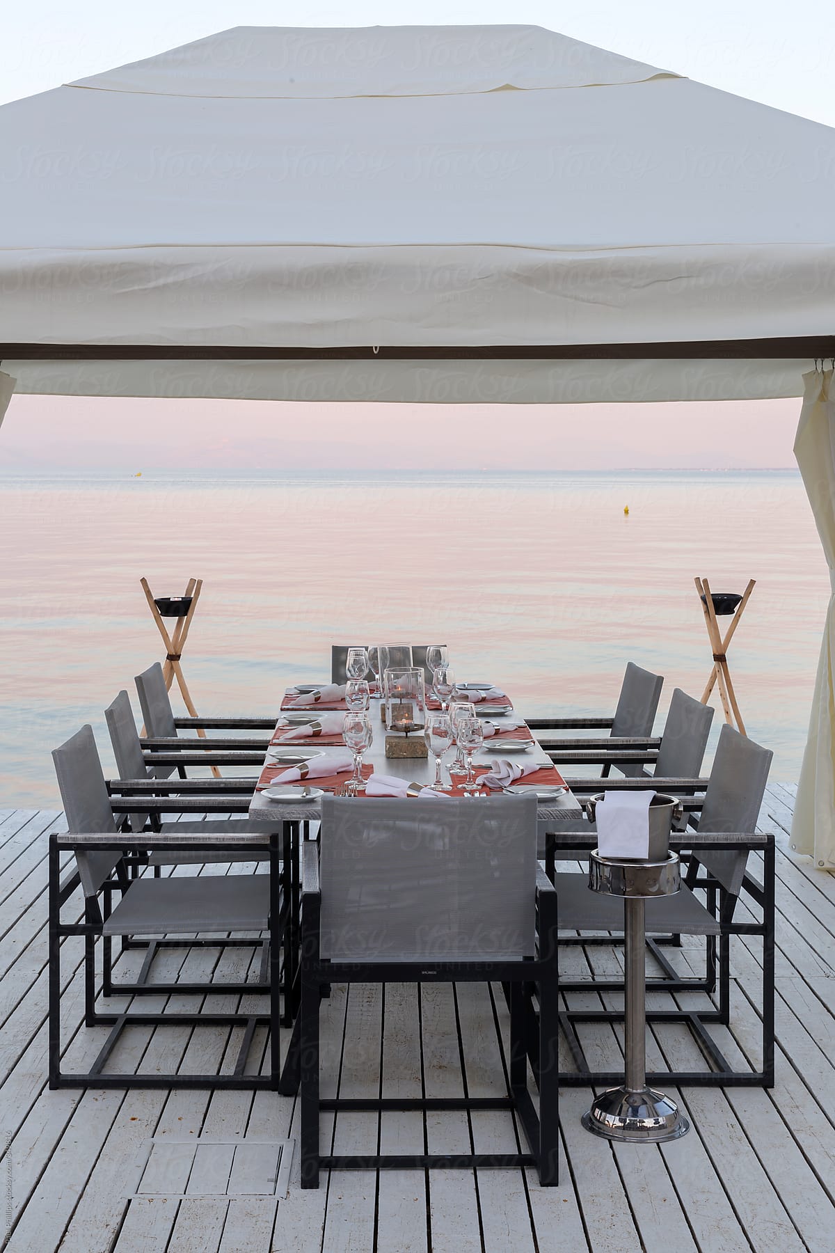 Table set for dinner on the edge of a beach at sunset under a white gazebo