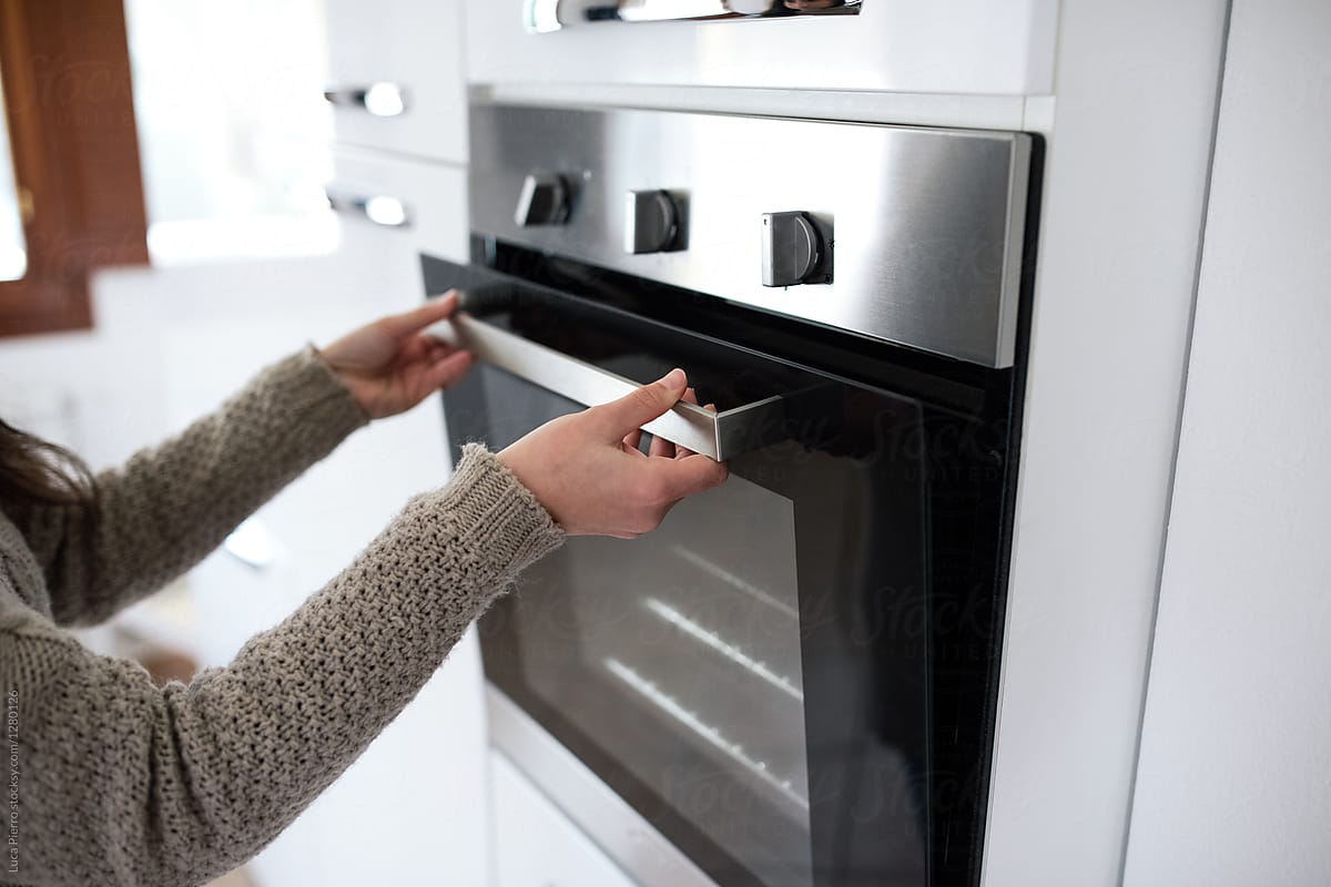 Female hand opening oven in white kitchen electric stove on gray background