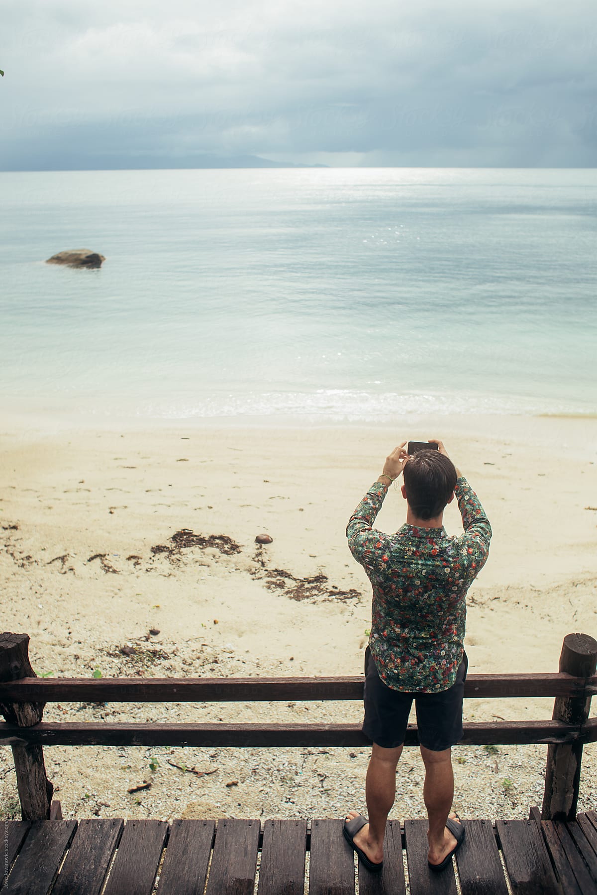 View of man from behind taking a picture of the beach