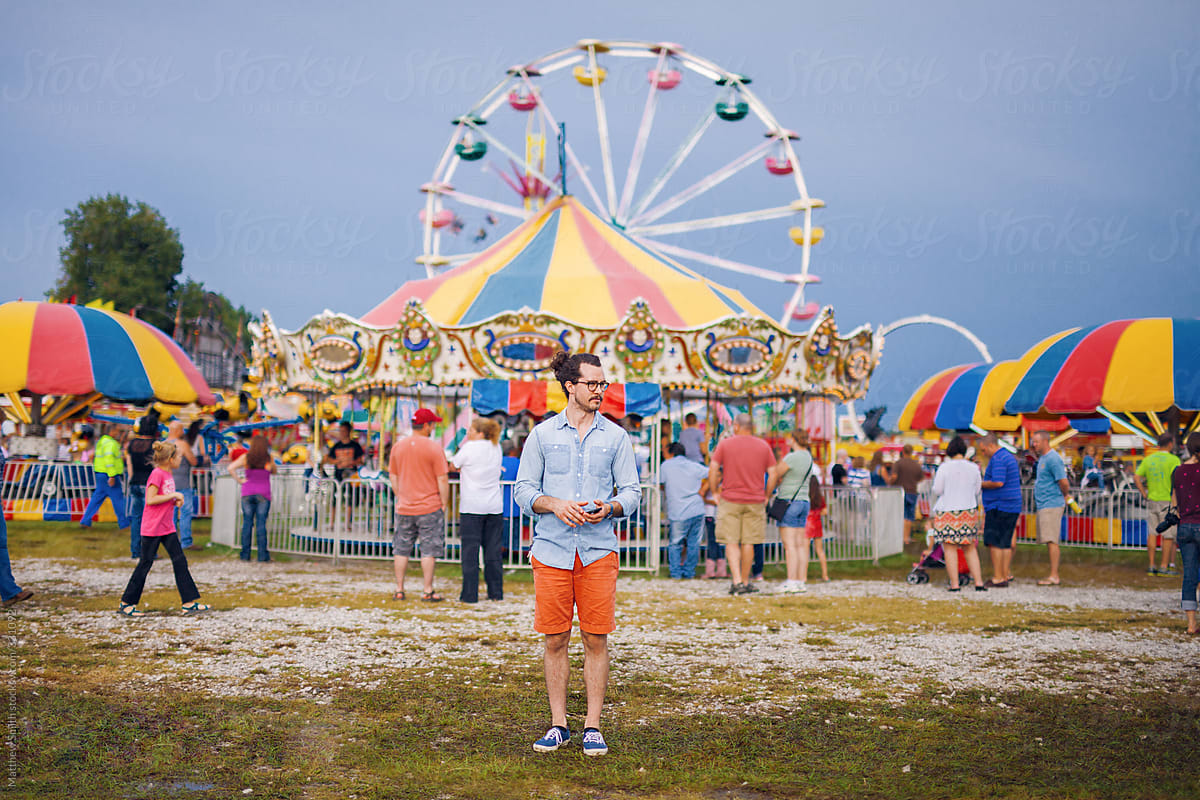 Man Standing in front of a Ferris Wheel At A Small Town Fair