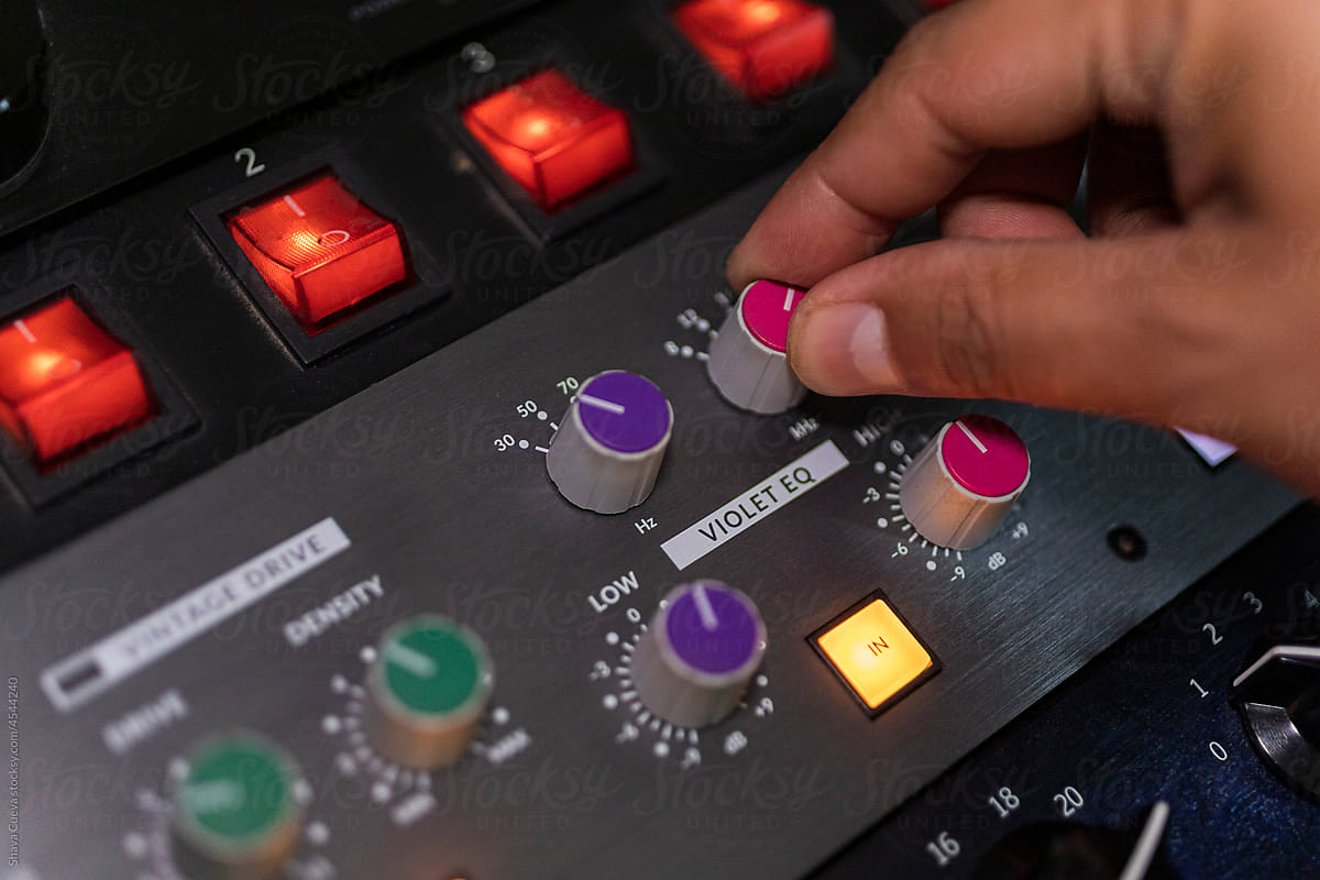 closeup of male right hand moving a volume dial on an audio console