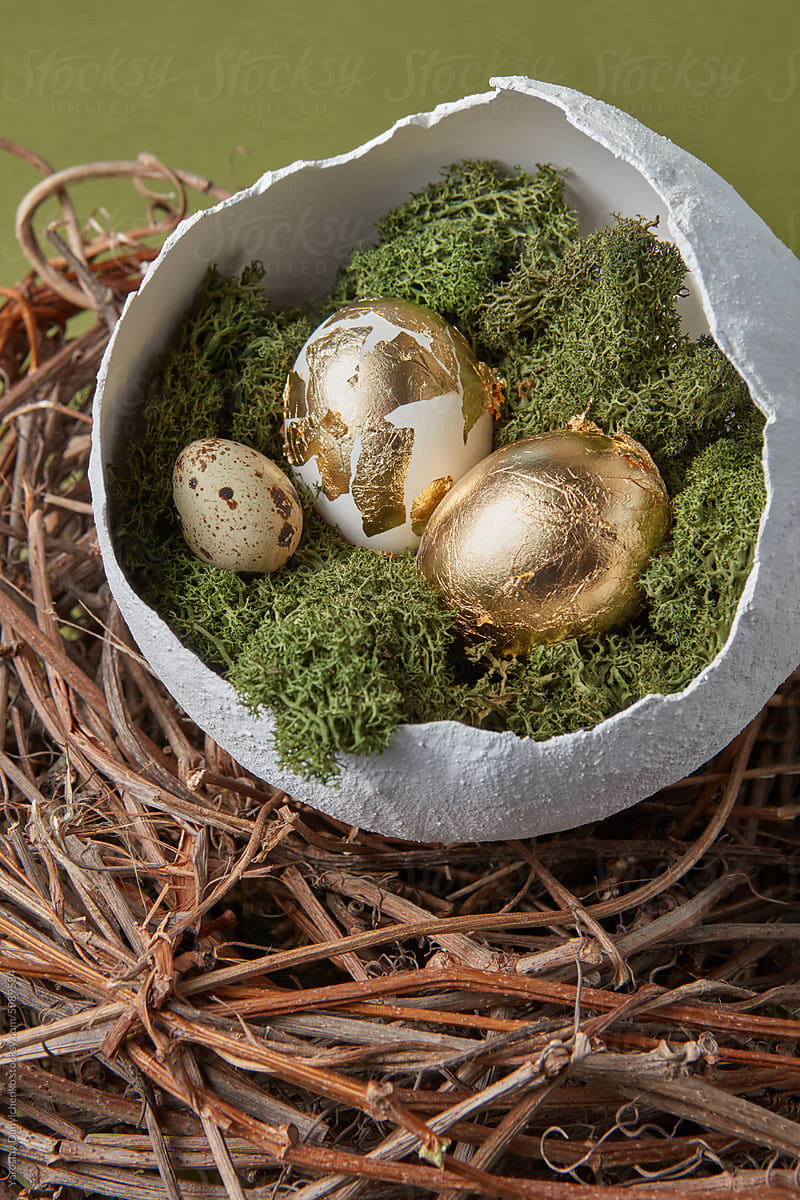 Eggs decorated with golden foil laying in white bowl on bird nest