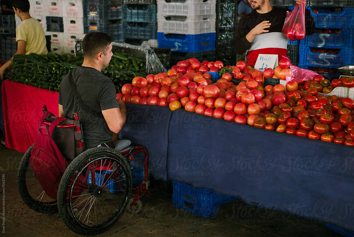Adult man on a wheelchair chooses fresh tomatoes at a street market