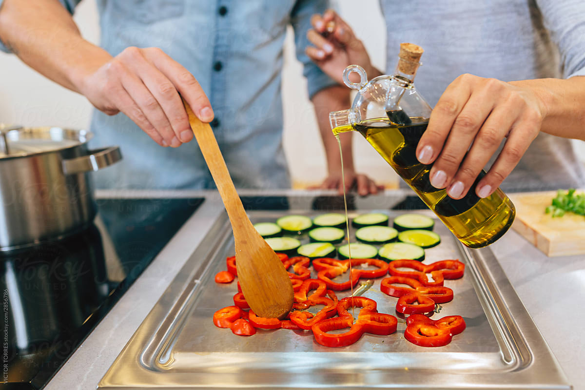 Anonymous couple pouring oil on peppers and zucchini