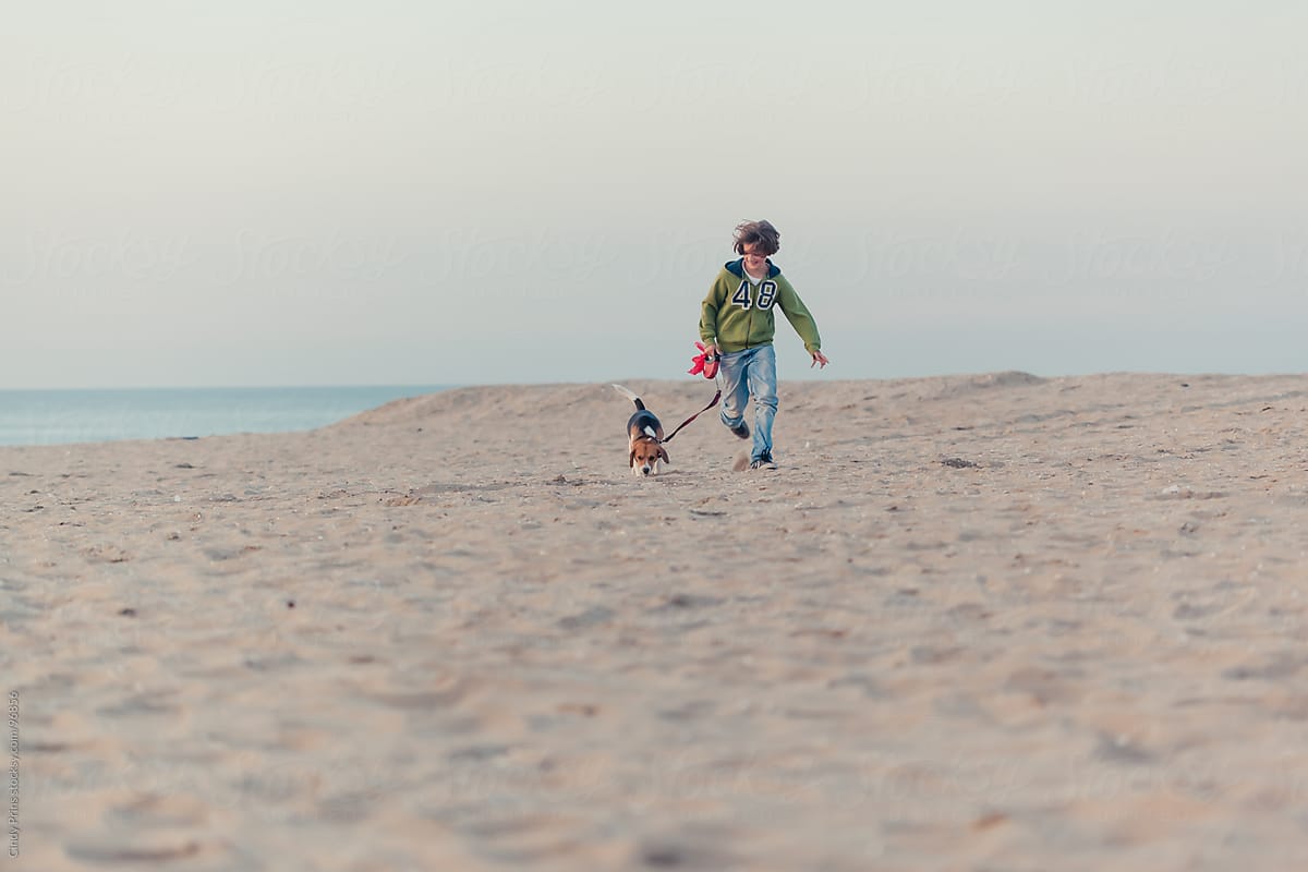 Boy running with a beagle dog on a leash on the beach