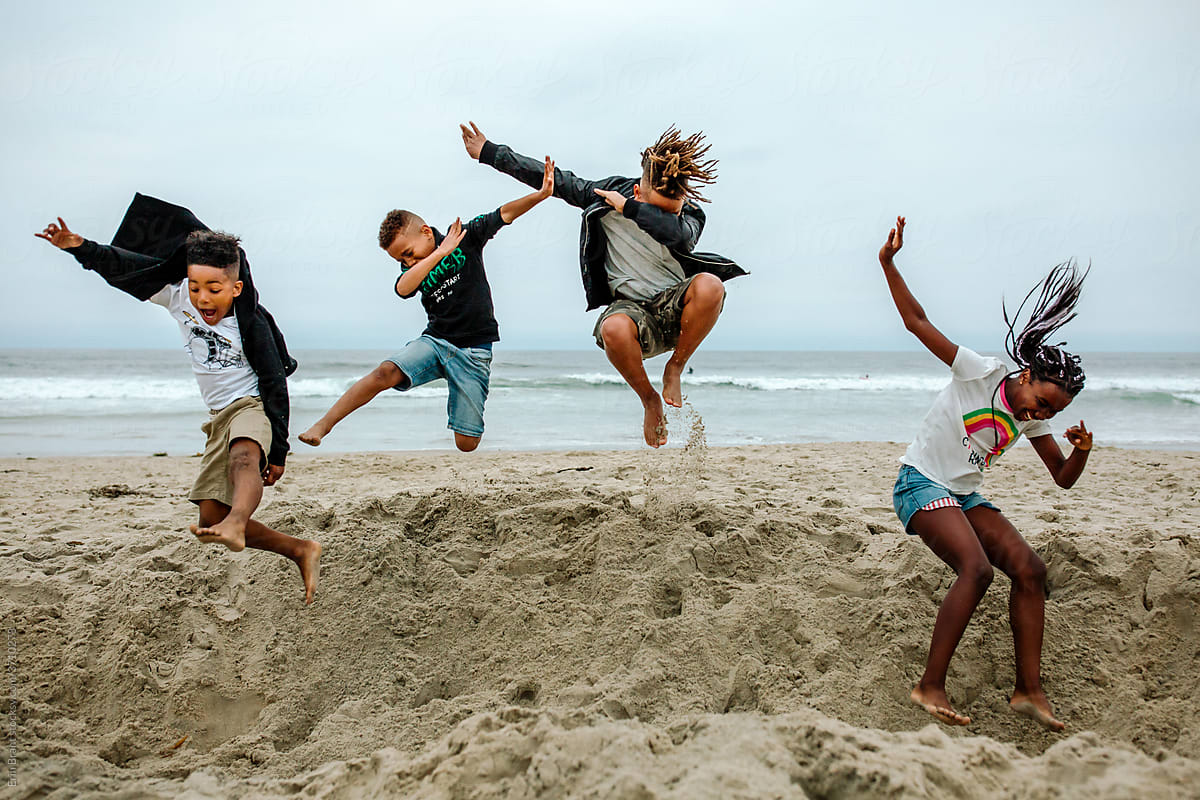 Siblings jumping together into sand crater