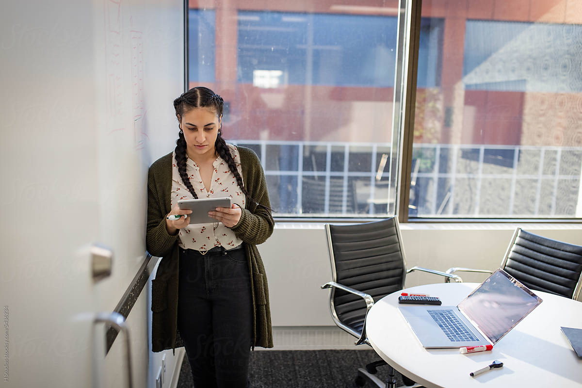 Young businesswoman with digital tablet at whiteboard in office