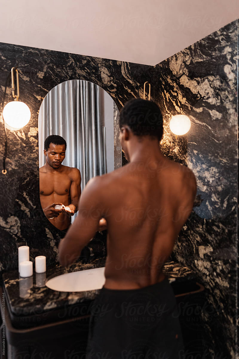 Shirtless Man Using A Skin Care Product In The Bathroom