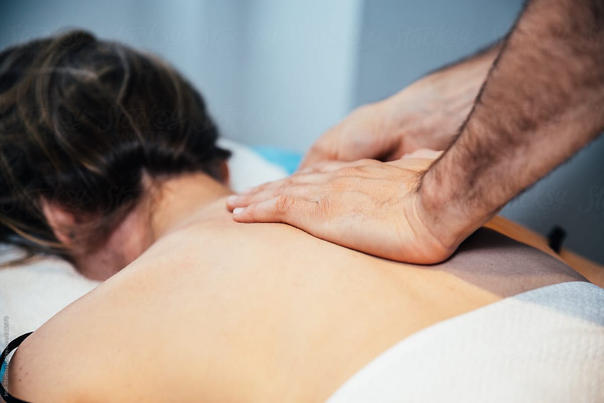 Young woman lying on her front on a bed receiving a massage on her shoulders by a male therapist